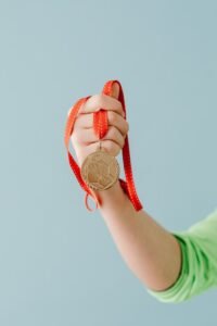 A close-up of a hand holding a gold medal with a red ribbon against a blue background.